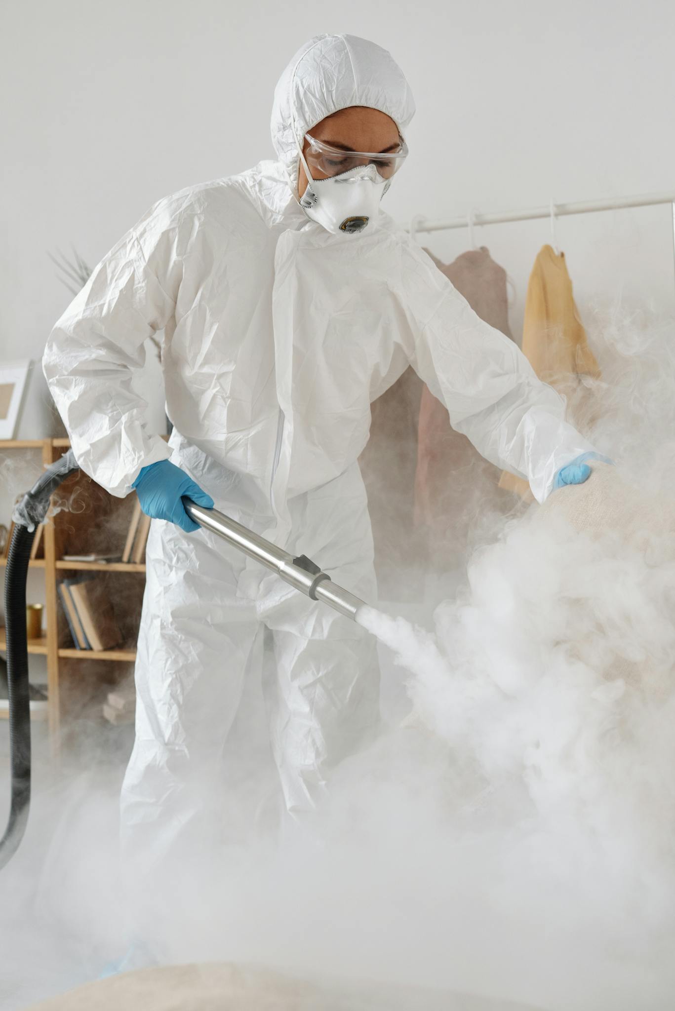 Person in PPE fumigates indoors with protective suit, gloves, and mask.
